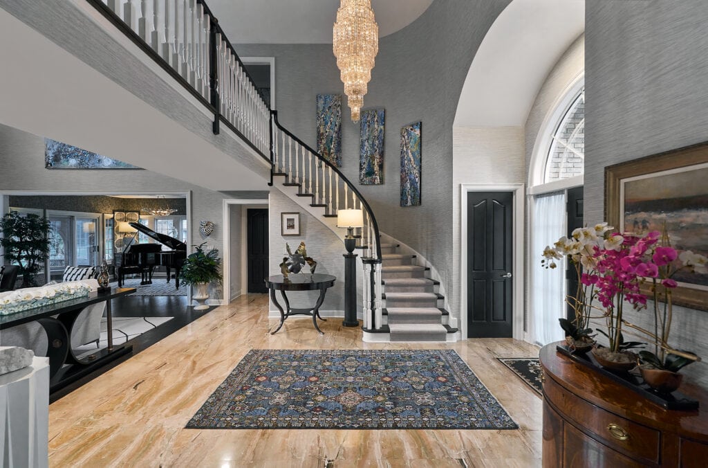 Large foyer with curved staircase, chandelier, and grand piano in background.