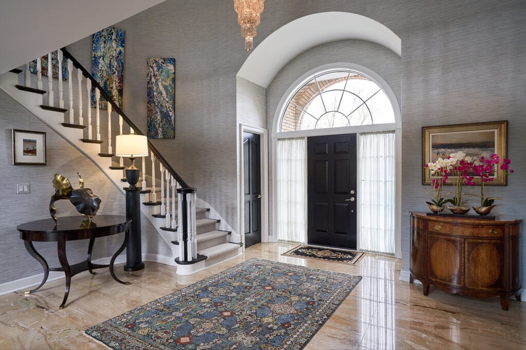 Entryway with curved staircase, arched window, and wooden sideboard.
