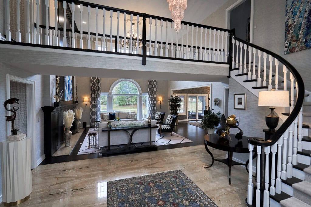 Entryway with curved staircase, two-story balcony, and patterned rug.