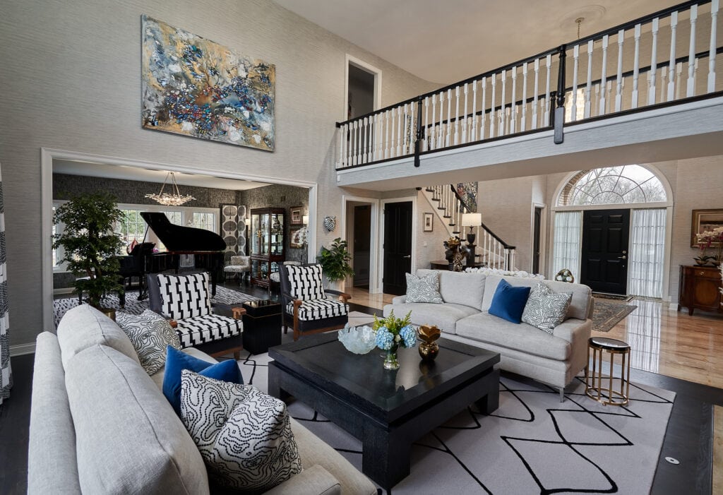 Two-story living room with grand piano, patterned chairs, and large artwork.