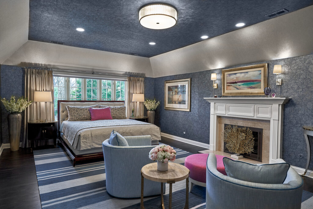 Bedroom with fireplace, artwork above, armchairs, and striped rug